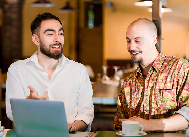 {"en":"Two men are sitting at a table in a cafe, engaged in a conversation. One man is wearing a white shirt, and the other is wearing a colorful patterned shirt. They look relaxed and are smiling, with a laptop and coffee cups in front of them.","de":"Zwei Mu00e4nner sitzen an einem Tisch in einem Cafu00e9 und fu00fchren ein Gespru00e4ch. Der eine Mann tru00e4gt ein weiu00dfes Hemd, der andere ein bunt gemustertes Hemd. Sie wirken entspannt und lu00e4cheln, vor ihnen befindet sich ein Laptop und Kaffeetassen."}